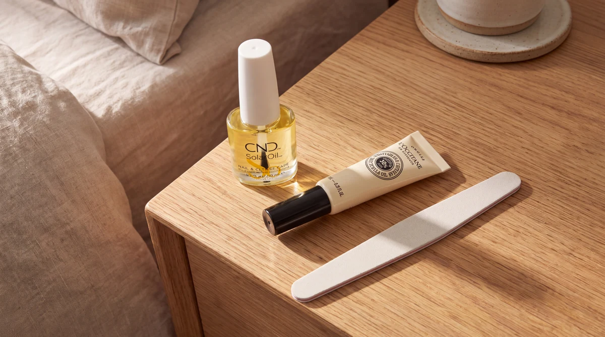 CND SolarOil and L'Occitane cuticle oil beside a nail file on a wooden bedside table