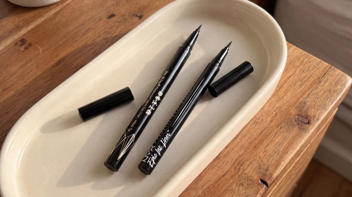Uncapped Stila and NYX liquid eyeliners in a cream ceramic tray on a wooden table